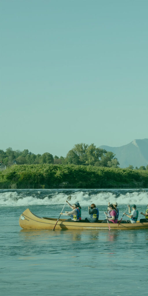six personnes sur un kayac dans un cours d'eau avec petite cascade en fond