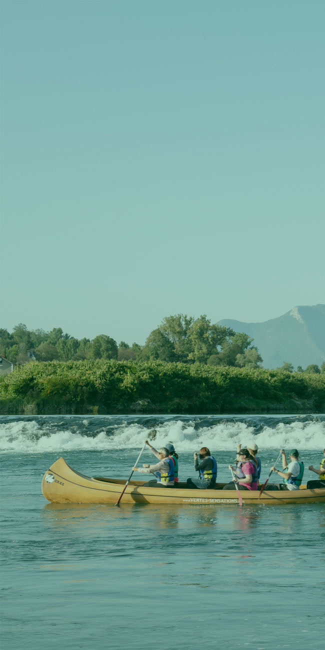 six personnes sur un kayac dans un cours d'eau avec petite cascade en fond